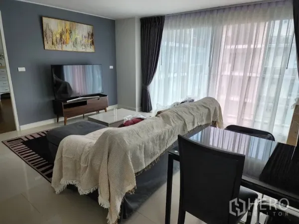 Condominium for rent in Watthana, Bangkok - Living room with TV console, sheer curtains, dark feature wall, and a four-seat dining set.