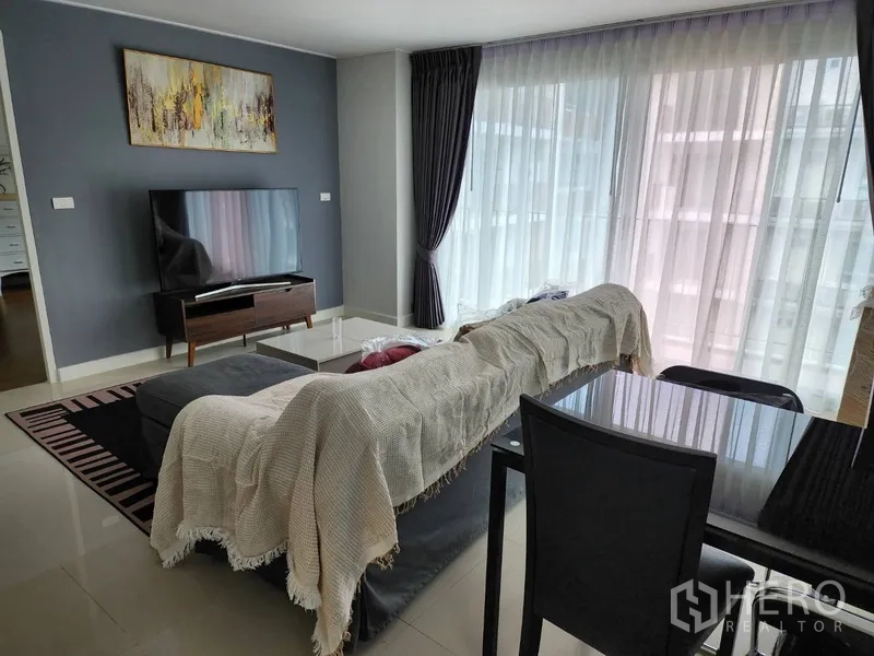 Condominium for rent in Watthana, Bangkok - Living room with TV console, sheer curtains, dark feature wall, and a four-seat dining set.