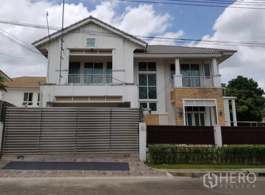Detached House for sale in Lat Krabang, Bangkok - Two-storey detached house in Lat Krabang, Bangkok with a tall metal sliding gate, balconies, large windows and brick accents on a paved driveway.