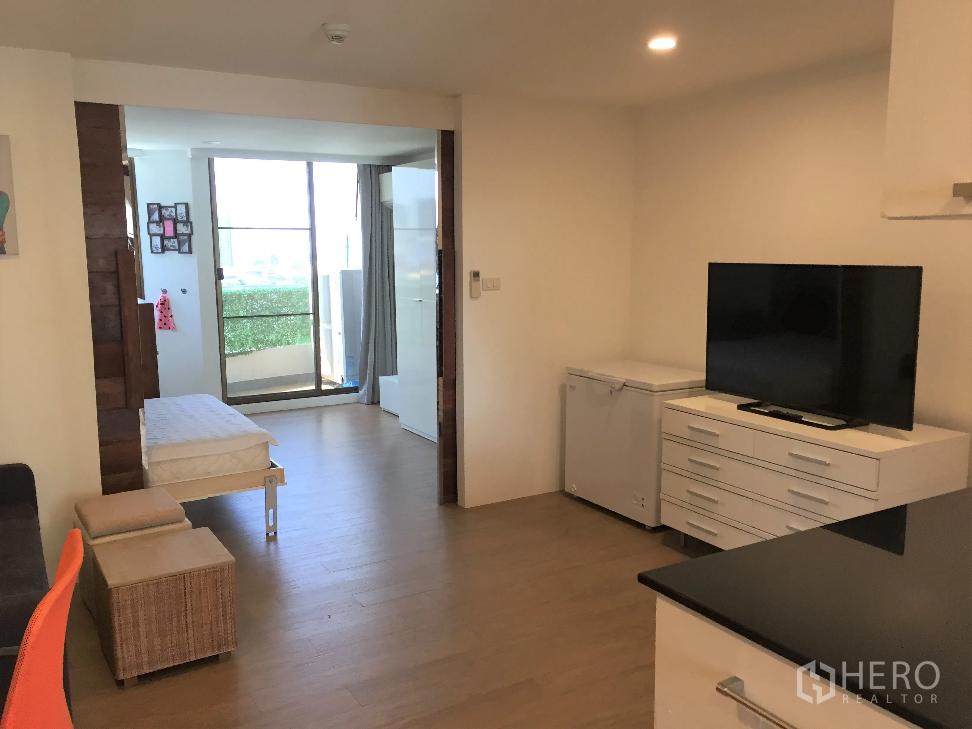 Condominium for rent in Watthana, Bangkok - Living area with TV console and seating, opening to a balcony through glass doors.