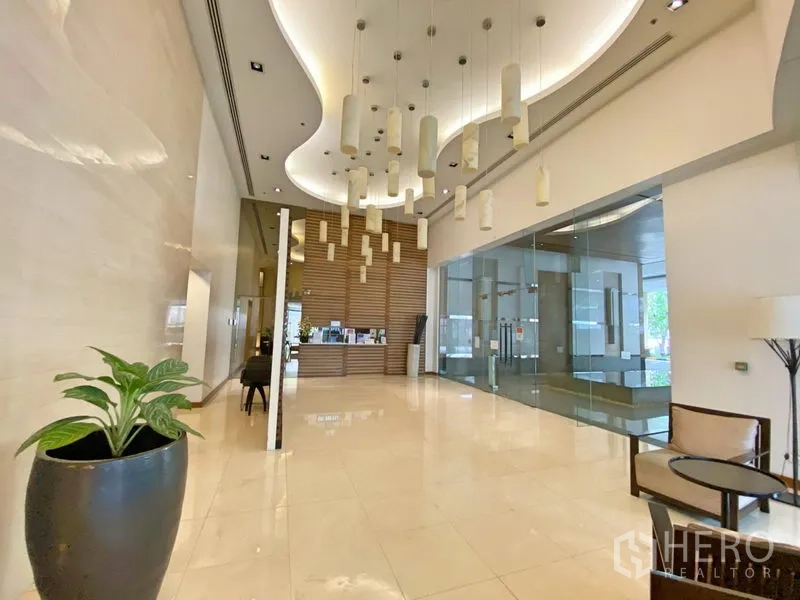 Condominium for rent in Khlong Toei, Bangkok - Modern condo lobby with high ceiling, pendant lights, reception desk and glass meeting room.