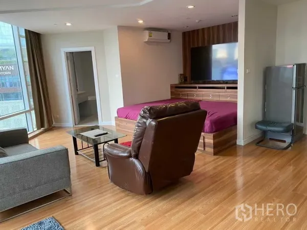 Condominium for rent in Pathum Wan, Bangkok - Bright open-plan living area with sofa, recliner, bed platform, TV wall and floor-to-ceiling windows.