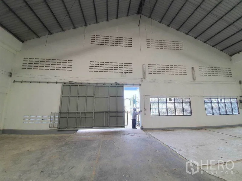 Warehouse for rent in Nakhon Pathom - Interior view toward a large sliding metal door beneath a ventilated gable wall.