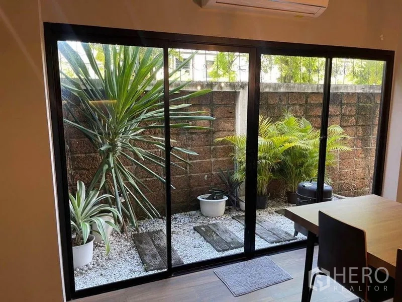 Townhouse for sale in Bang Phli, Samut Prakan - Private pocket garden with potted plants and gravel path viewed through sliding glass doors.