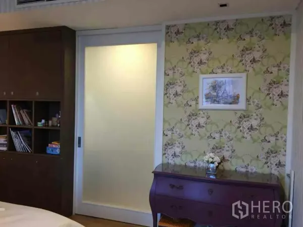 Condominium for rent or sale in Watthana, Bangkok - Bedroom wall with floral wallpaper, a frosted sliding door and a classic dresser in a Bangkok condo.