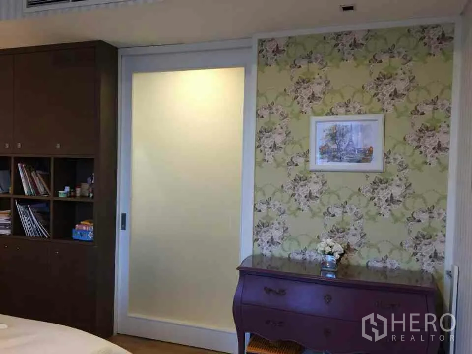 Condominium for rent or sale in Watthana, Bangkok - Bedroom wall with floral wallpaper, a frosted sliding door and a classic dresser in a Bangkok condo.