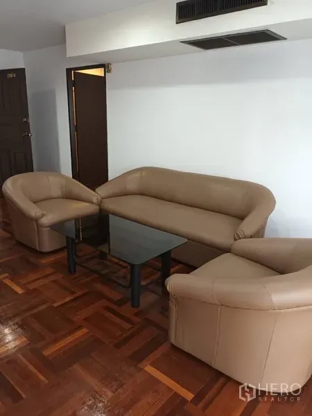 公寓 出租在Din Daeng, Bangkok - 三件式米色皮沙发围绕黑色玻璃茶几，木地板温馨客厅。