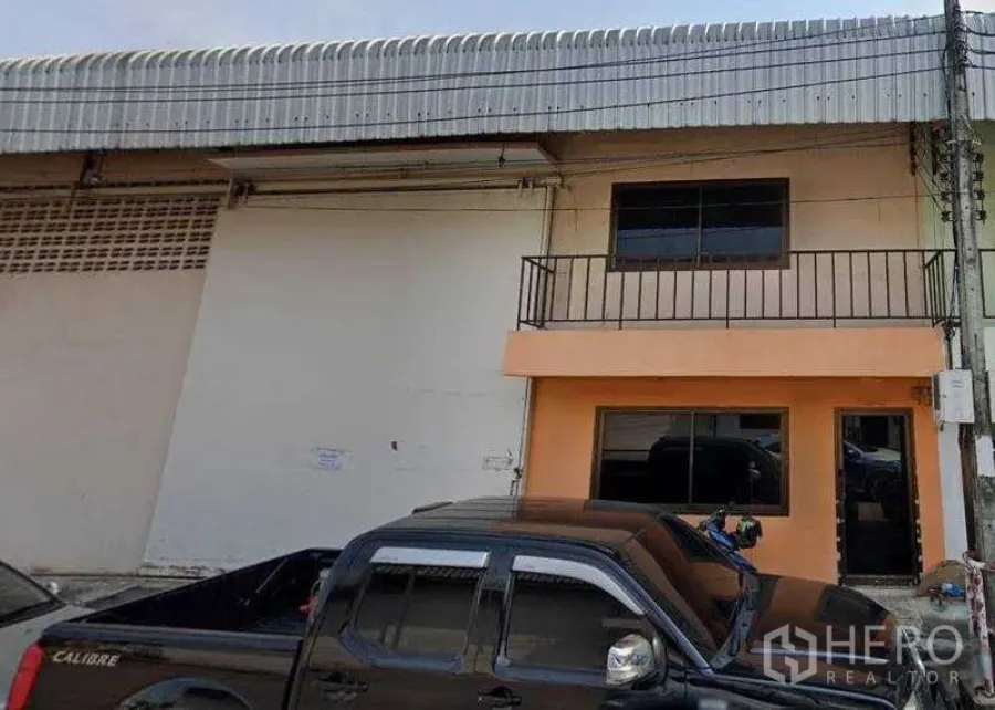 Warehouse for rent in Nong Khaem, Bangkok - Two-storey warehouse facade with balcony, wide windows, and parking space in front.
