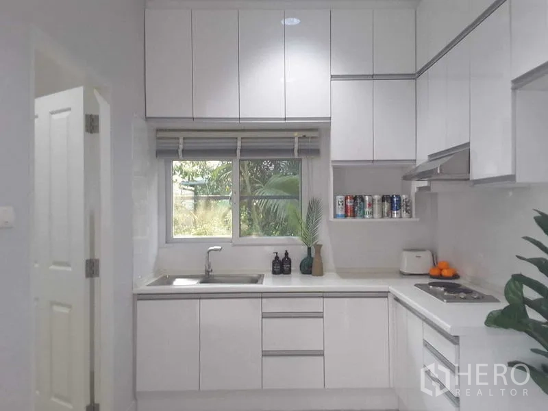 Detached House for rent in Lam Luk Ka, Pathum Thani - Modern white built-in kitchen with cabinets, window and cooktop.