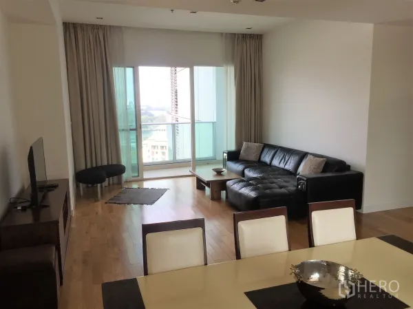 Condominium for rent in Khlong Toei, Bangkok - Open-plan lounge and dining space with floor-to-ceiling windows, balcony, and L-shaped sofa.