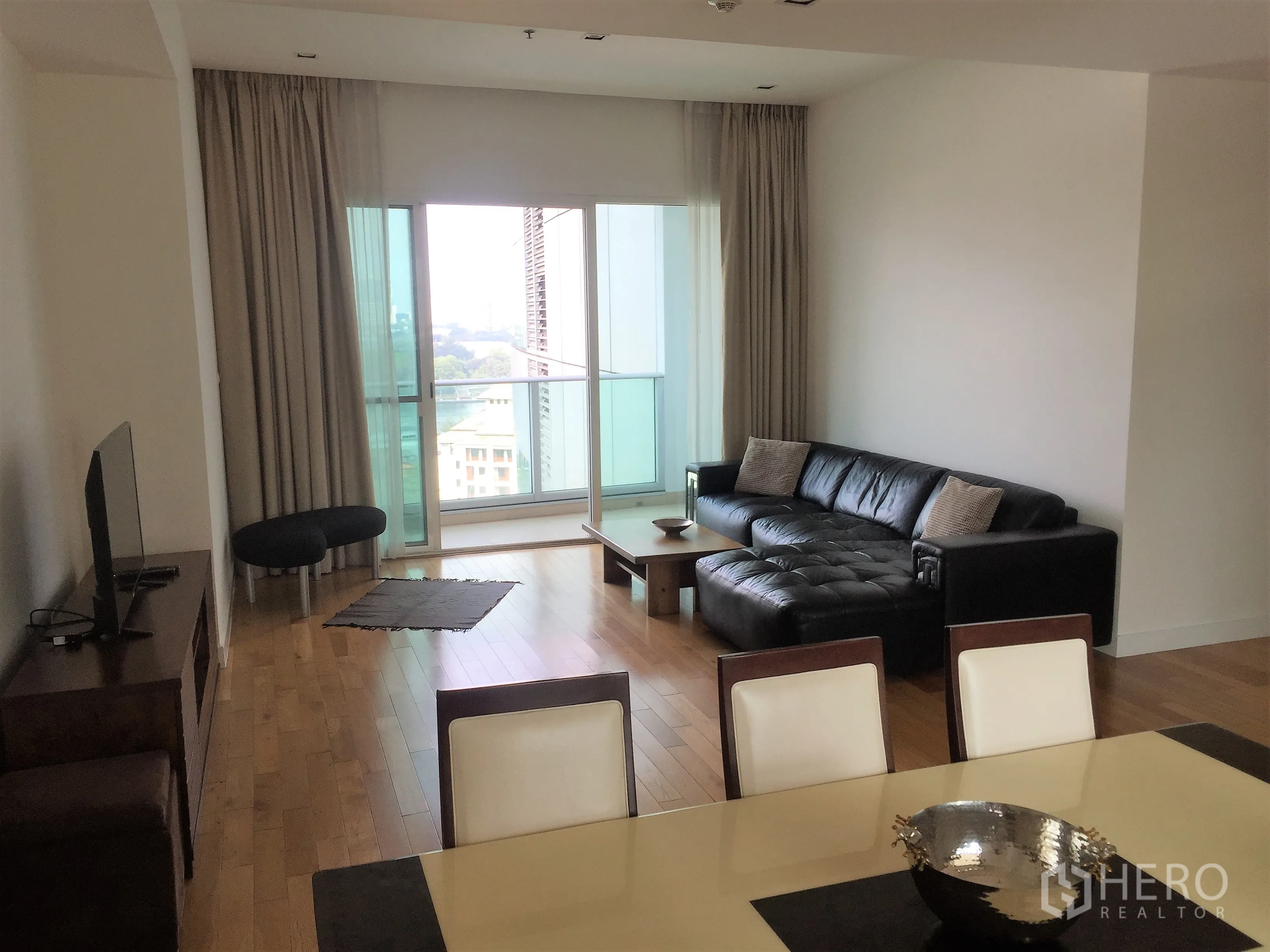 Condominium for rent in Khlong Toei, Bangkok - Open-plan lounge and dining space with floor-to-ceiling windows, balcony, and L-shaped sofa.