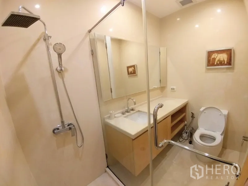 Condominium for rent in Chatuchak, Bangkok - Modern bathroom with glass shower, rain head, large mirror, and vanity beside the toilet.