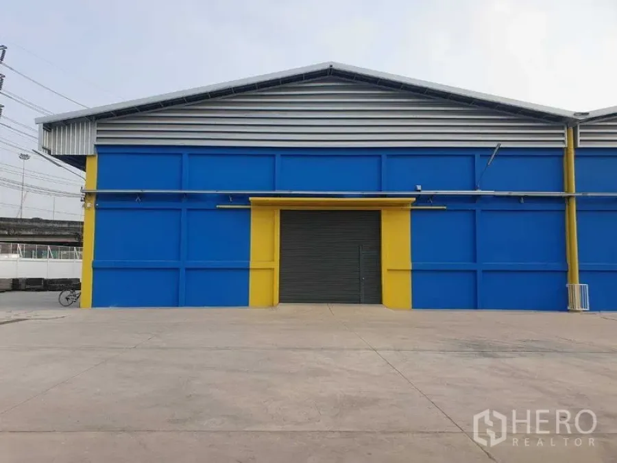 货栈 出租在Khlong Luang, Pathum Thani - 蓝色仓库正立面，黄色门框，前方宽敞硬化场地。