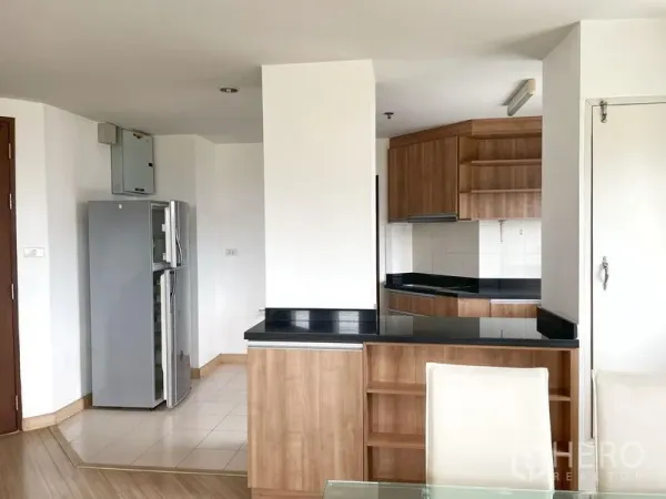 Condominium for rent in Khlong Toei, Bangkok - Open kitchen entry with breakfast counter, wood cabinetry, black countertops and a double-door refrigerator.