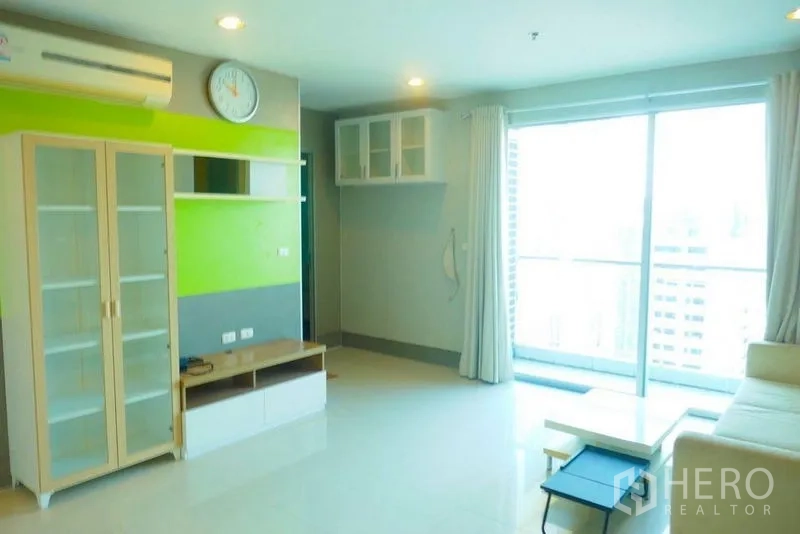 Condominium for rent or sale in Khlong San, Bangkok - Living area opening to balcony via large sliding doors with glass cabinet nearby.