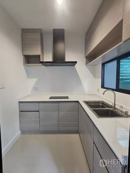 Townhouse for rent in Saphan Sung, Bangkok - Compact L-shaped kitchen with wood cabinets, cooktop, range hood and a window.