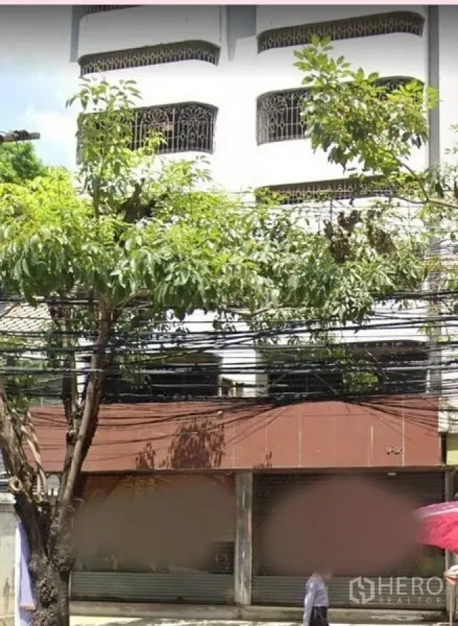 อาคารพาณิชย์ ให้เช่าในWatthana, Bangkok - ด้านหน้าตึกอาคารพาณิชย์หลายชั้น มีต้นไม้และประตูม้วนหน้าร้าน
