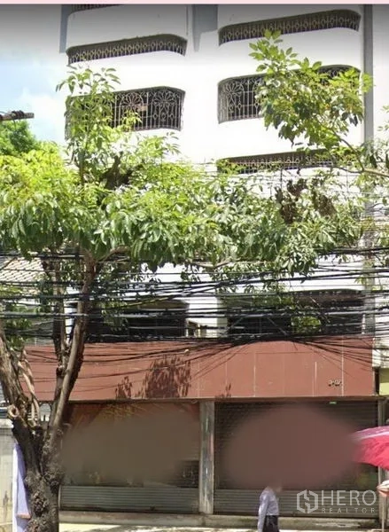 อาคารพาณิชย์ ให้เช่าในWatthana, Bangkok - ด้านหน้าตึกอาคารพาณิชย์หลายชั้น มีต้นไม้และประตูม้วนหน้าร้าน