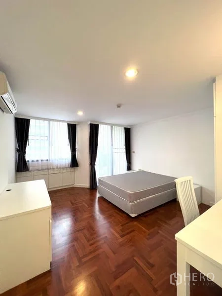 公寓 出租在Watthana, Bangkok - 卧室铺设拼花木地板，设大窗与深色窗帘、平台床与书桌。
