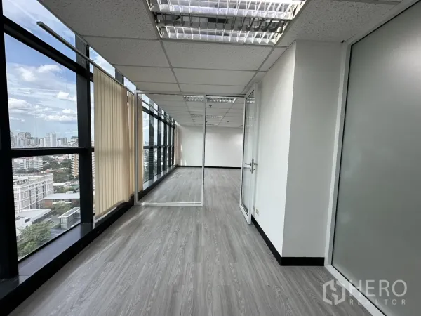 办公空间 出租在Watthana, Bangkok - 临窗走道设百叶，通向玻璃门会议室，可见城市景观。