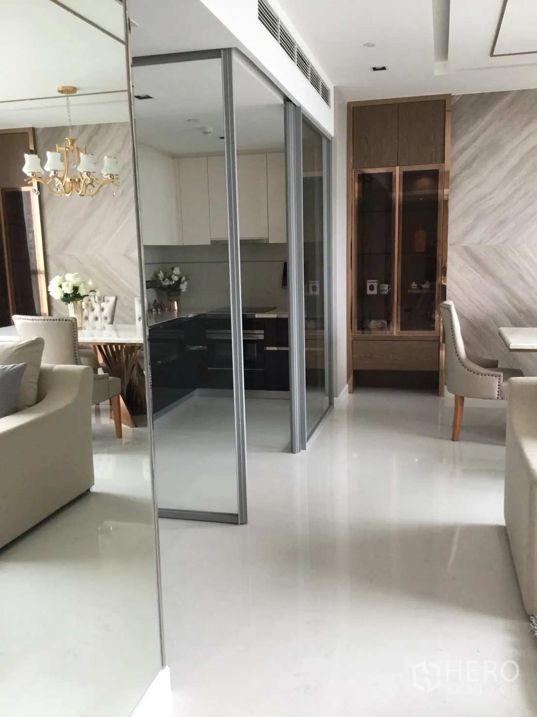 Condominium for rent in Sathon, Bangkok - Hallway with mirrored wall and glass sliding doors leading to a modern enclosed kitchen with built-in cabinetry.