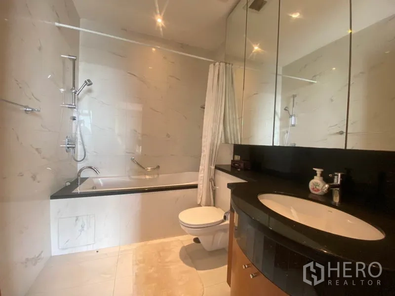 Condominium for rent in Sathon, Bangkok - Secondary bathroom with bathtub and shower combination, black stone vanity and mirrored cabinets.