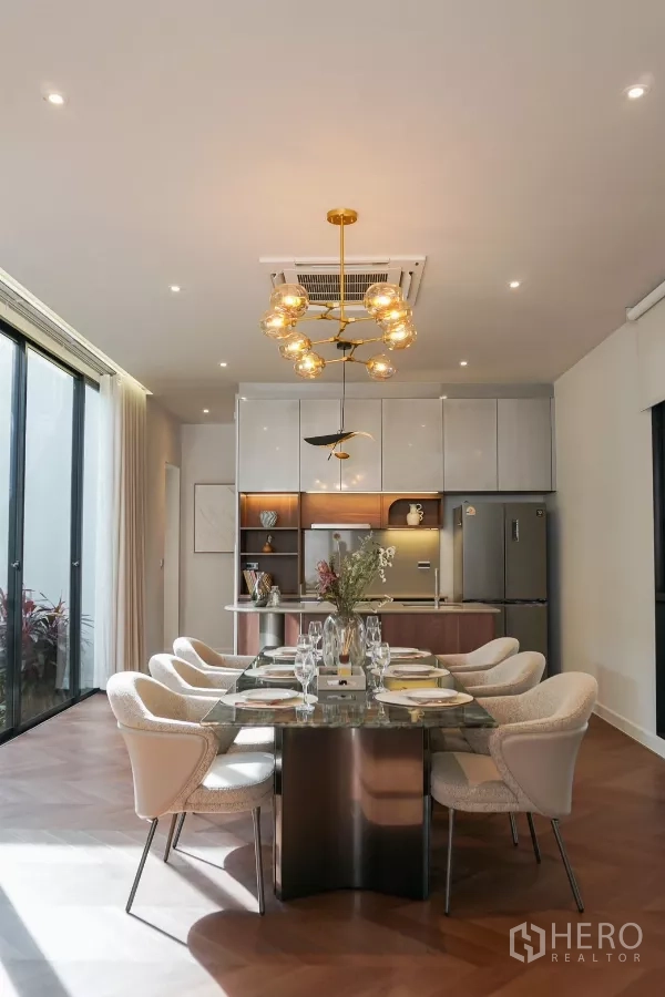 Detached House for rent or sale in Bang Kapi, Bangkok - Dining room under a sculptural gold chandelier facing a sleek fitted kitchen.