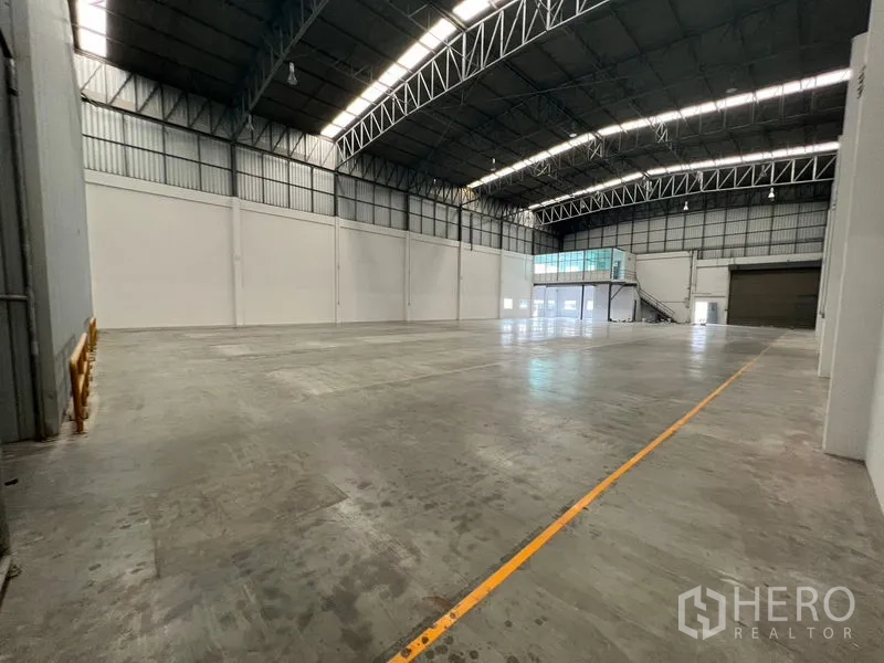 Warehouse for rent in Lat Krabang, Bangkok - Large clear-span warehouse floor with marked lanes, mezzanine glass office, and multiple loading doors.