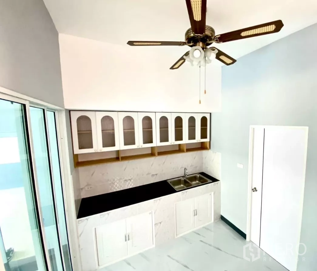 Factory for rent or sale in Bang Bua Thong, Nonthaburi - Kitchen view highlighting ceiling fan and ample cabinet storage.