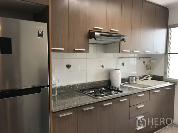 公寓 出租在Watthana, Bangkok - 独立厨房，木质橱柜、花岗岩台面、燃气灶与不锈钢冰箱。
