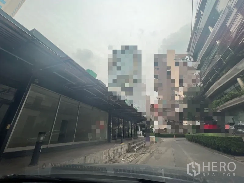 Retail Space for rent in Khlong Toei, Bangkok - Row of glass-fronted retail spaces with a long awning and driveway, with high-rises in the Phrom Phong area.