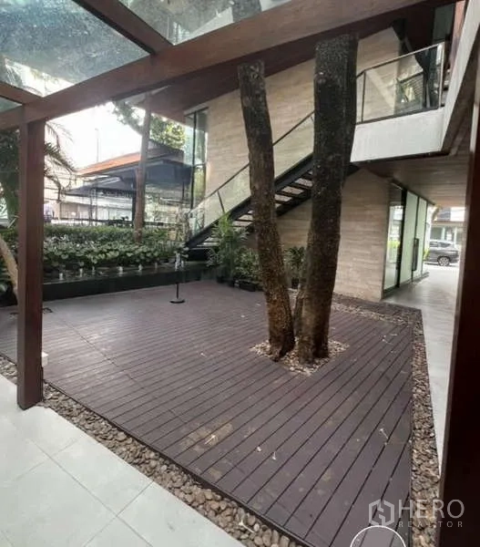 零售空间 出租在Watthana, Bangkok - 带玻璃雨棚的露台，木平台围树，旁有室外楼梯。