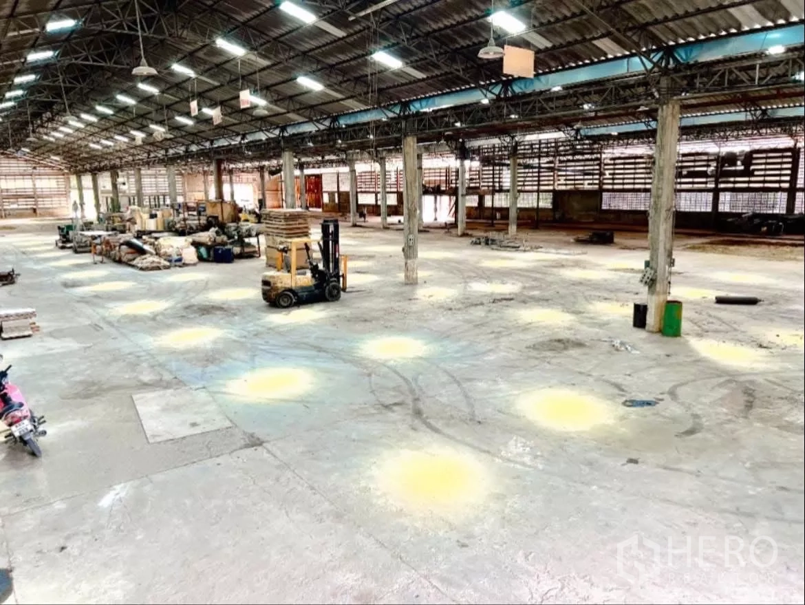 Factory for rent in Sai Noi, Nonthaburi - Open warehouse floor with forklifts and storage areas beneath the lit roof.