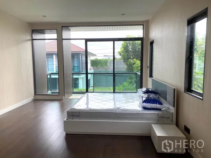 Detached House for rent in Saphan Sung, Bangkok - Large bedroom with bed and a full-height glass wall opening to a balcony view.