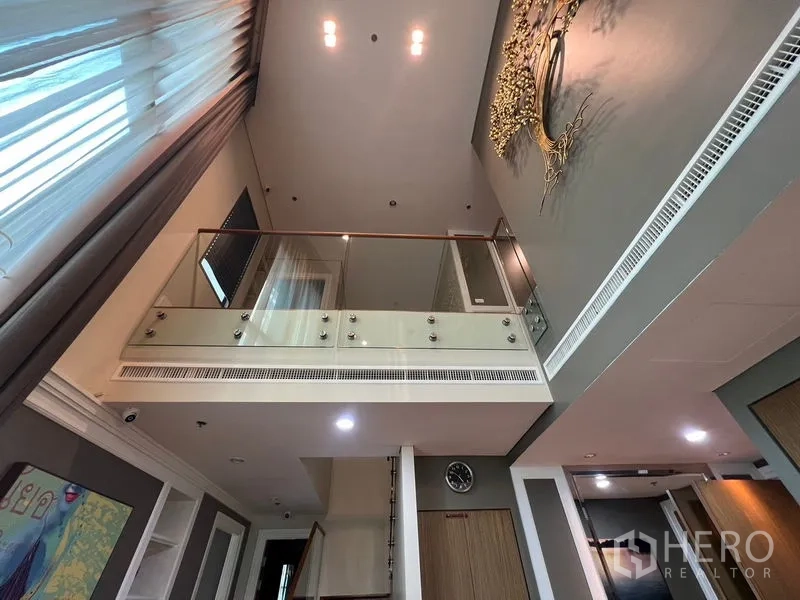 Condominium for rent in Khlong Toei, Bangkok - Mezzanine with glass balustrade overlooking the living area and a decorative wall art piece.