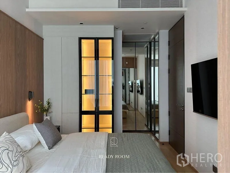 Condominium for rent in Pathum Wan, Bangkok - Bedroom with illuminated glass display wardrobe, mirrored closets and soft bedding.