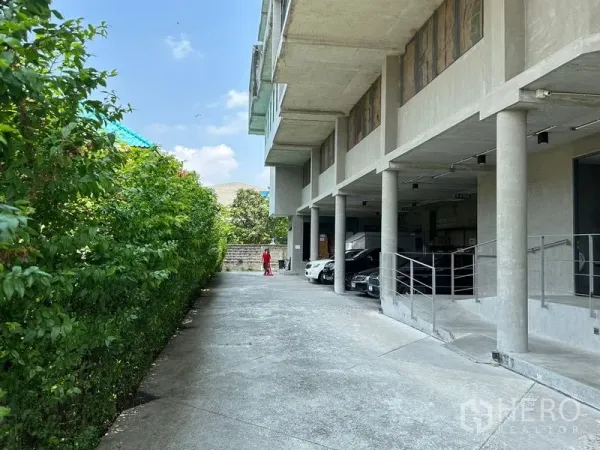 带办公室的家 出租或出售在Prawet, Bangkok - 沿绿篱的长车道，建筑下方设有遮棚停车位。