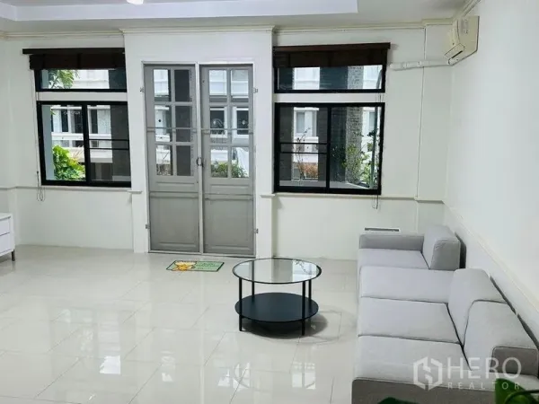 Home Office for rent in Watthana, Bangkok - Bright living room with gray sofa, round glass coffee table, and double doors to a balcony.