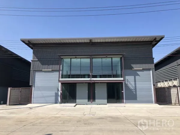 Warehouse for rent in Bang Phli, Samut Prakan - Modern grey warehouse facade with glass-fronted office, twin roller shutters and wide concrete apron.