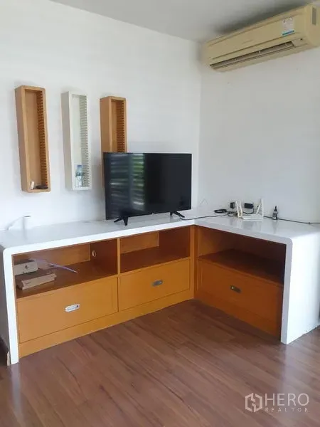 Townhouse for rent or sale in Yan Nawa, Bangkok - TV corner with L-shaped built-in cabinet, wooden flooring and wall-mounted air conditioner.