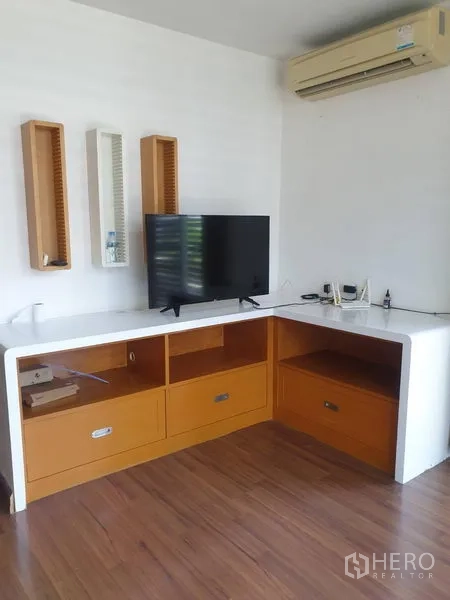 Townhouse for rent or sale in Yan Nawa, Bangkok - TV corner with L-shaped built-in cabinet, wooden flooring and wall-mounted air conditioner.