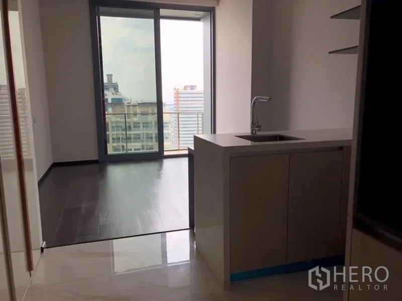 公寓 出售在Watthana, Bangkok - 开放式客厅，深色木地板，紧凑厨房，推拉玻璃门通往带城市景观的阳台。