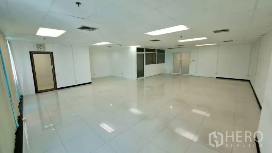 Office Space for rent in Huai Khwang, Bangkok - Bright open-plan 100 sqm office with white tile floors, T-bar ceiling, recessed lights, glass-partitioned room and double glass doors near MRT Sutthisan.