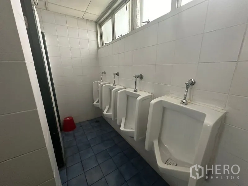Office Space for rent - Row of wall-mounted urinals beneath high windows in a tiled restroom