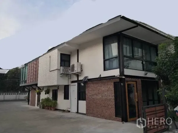 零售空间 出租在Khlong Toei, Bangkok - 两层商业建筑，白色与红砖立面，大面积窗户及车道停车区。