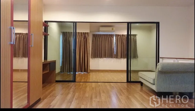 Townhouse for rent in Suan Luang, Bangkok - Spacious upper floor with wood flooring, built-in wardrobe, glass partition, and curtained windows.