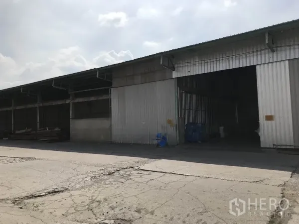 Warehouse for rent in Mueang Pathum Thani, Pathum Thani - Corrugated metal warehouse facade with multiple loading bays and a wide driveway for vehicles.