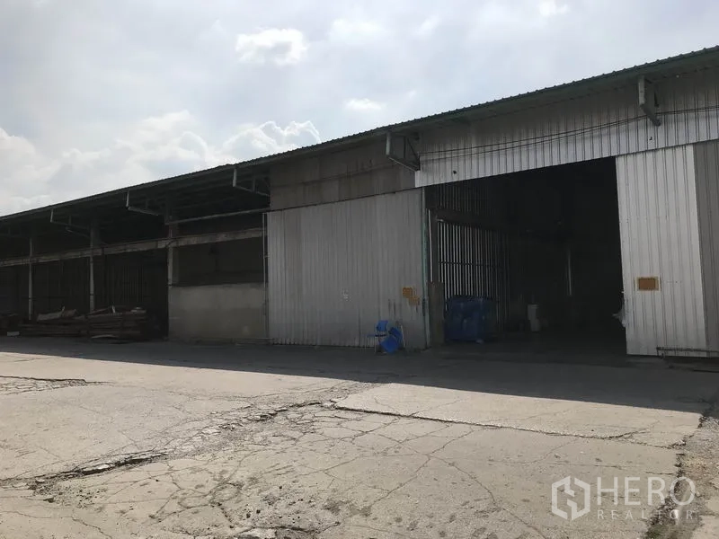 Warehouse for rent in Mueang Pathum Thani, Pathum Thani - Corrugated metal warehouse facade with multiple loading bays and a wide driveway for vehicles.