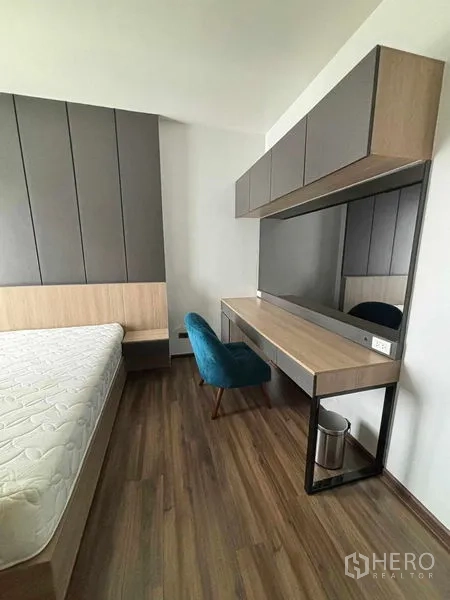 Condominium for rent or sale in Watthana, Bangkok - Bedroom corner with bed, long work desk, mirror and teal chair.