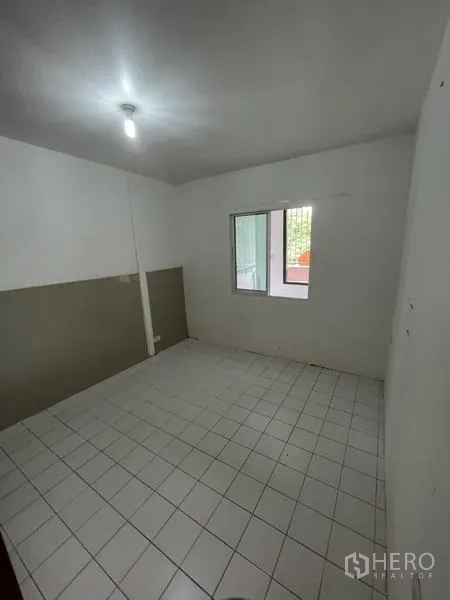 Shophouse for rent in Khlong Toei, Bangkok - Simple room with white floor tiles, small window, and ceiling light.